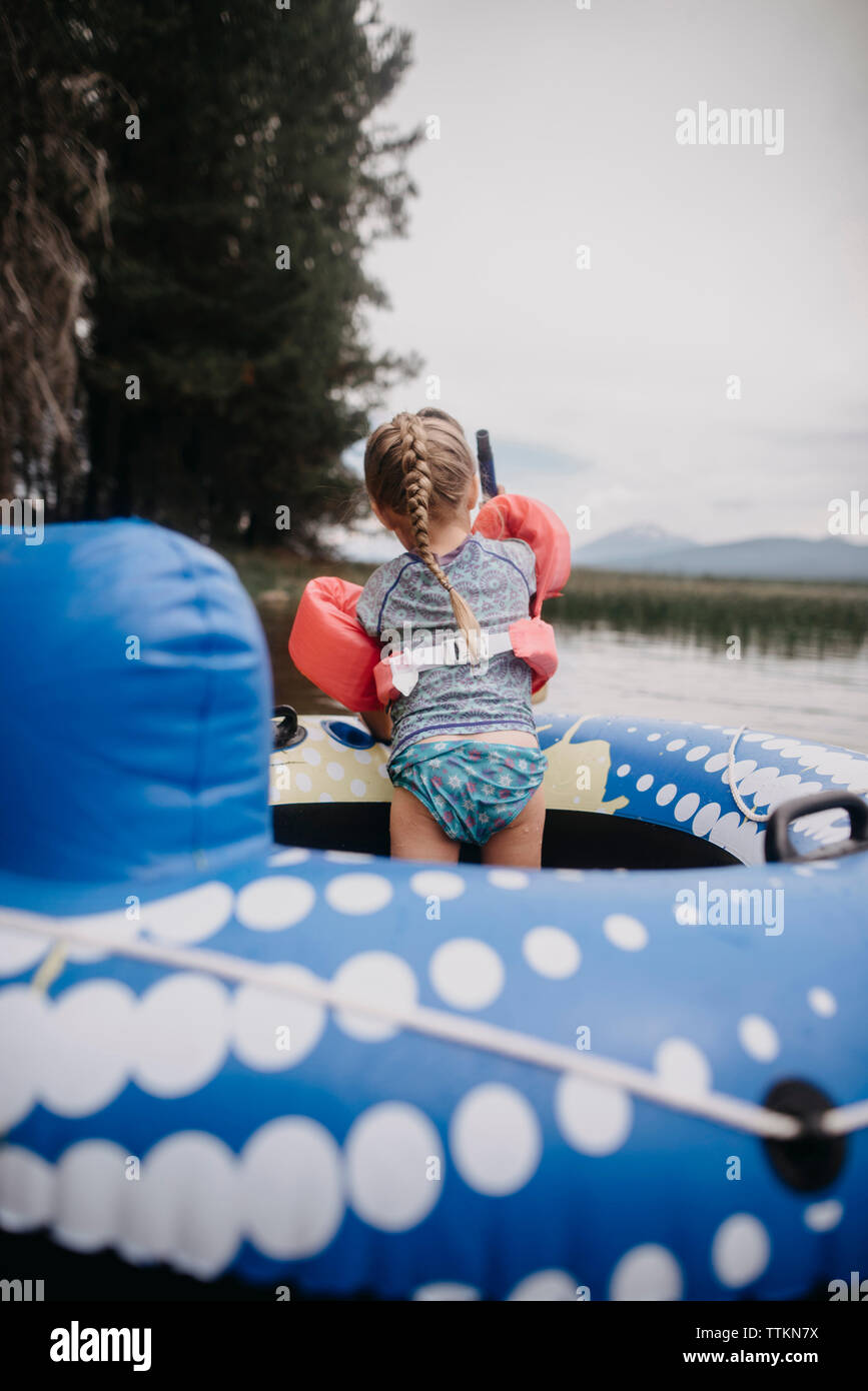 Rear view of girl with water wings standing in inflatable raft on lake Stock Photo