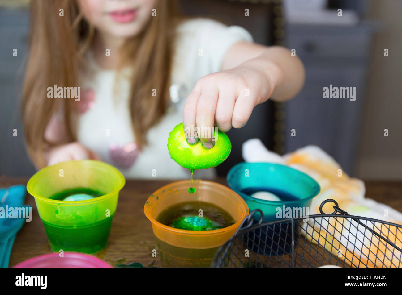 Midsection of girl dipping easter Egg in dyed water on table at home Stock Photo