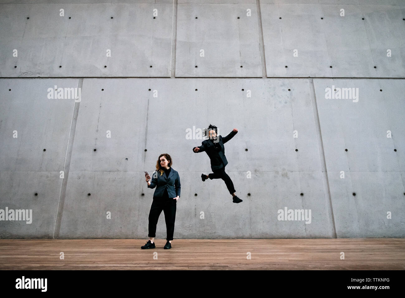 Man in mid-air while woman using phone against wall Stock Photo