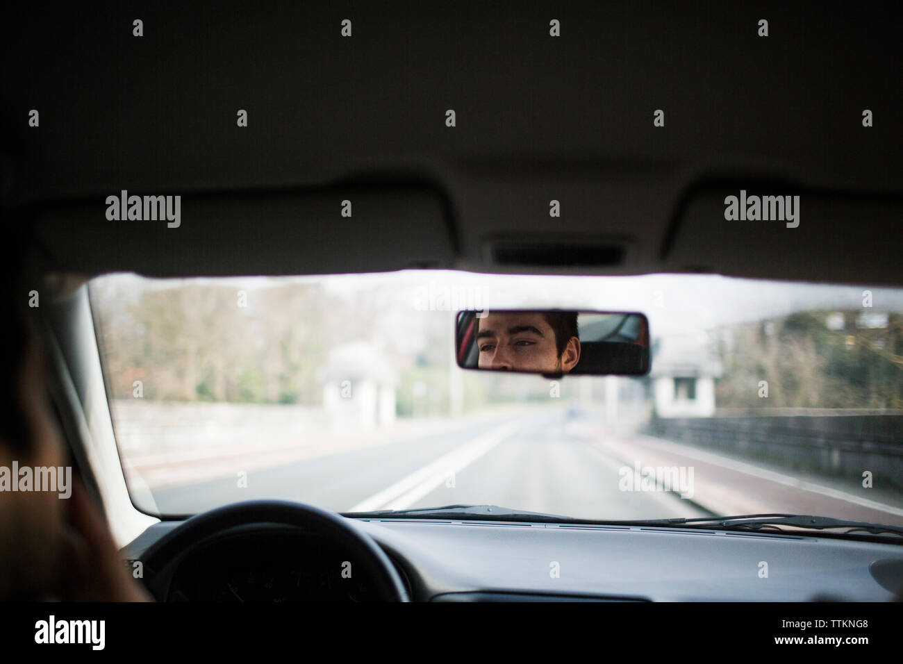 Reflection of man in car rear-view mirror on road Stock Photo