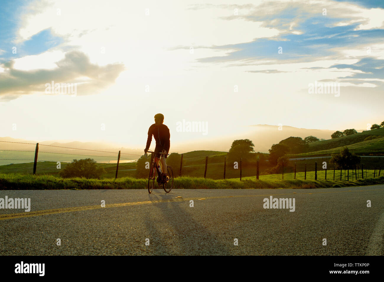 Young man cycling on street against cloudy sky Stock Photo