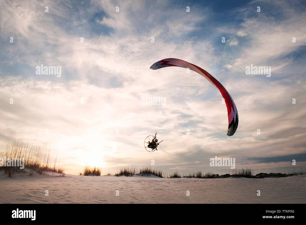 Man paragliding over sandy beach against sky Stock Photo