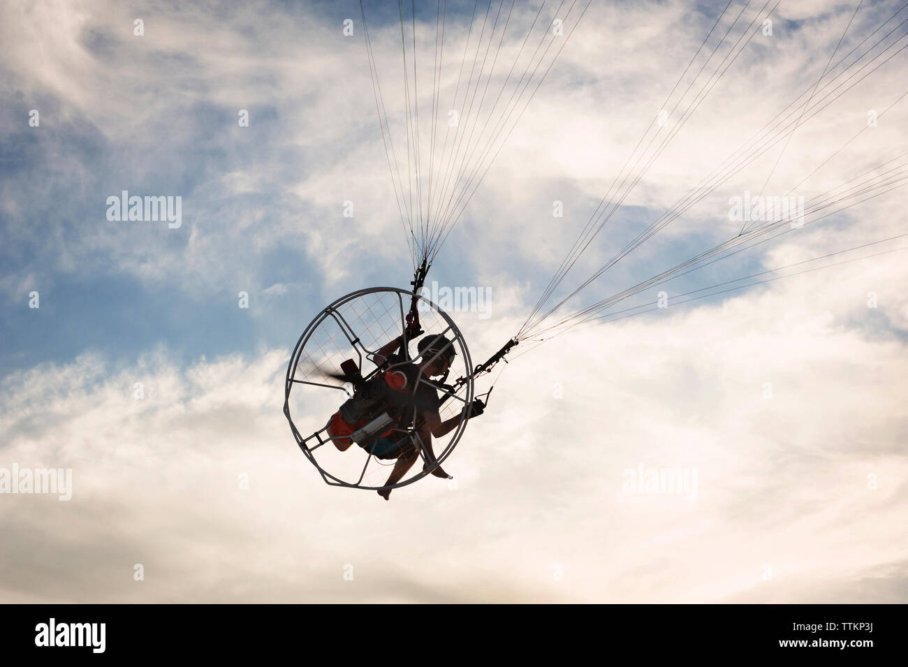 Low angle view of man paragliding against cloudy sky Stock Photo