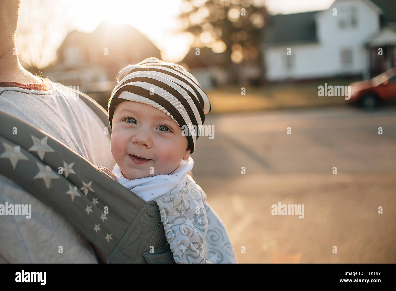 Midsection of father carrying daughter in baby sling while standing on street during sunset Stock Photo
