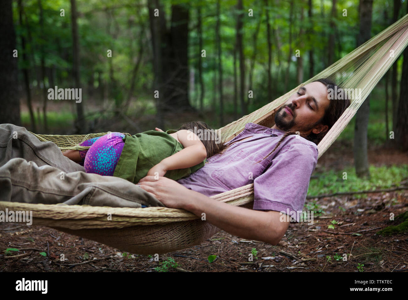 Father and daughter sleeping on hammock in forest Stock Photo