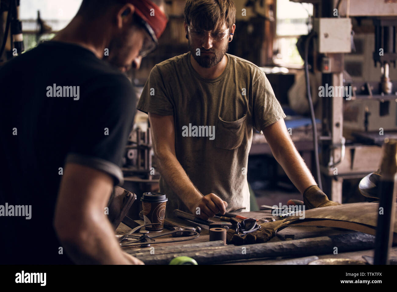 Blacksmith looking at coworker working at table in workshop Stock Photo