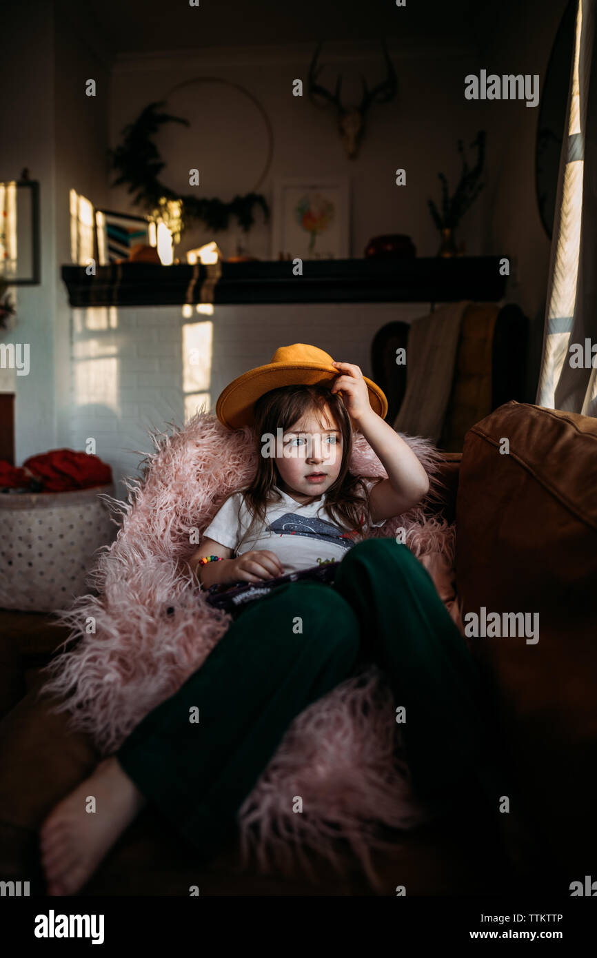 Girl looking out window with yellow hat in home Stock Photo