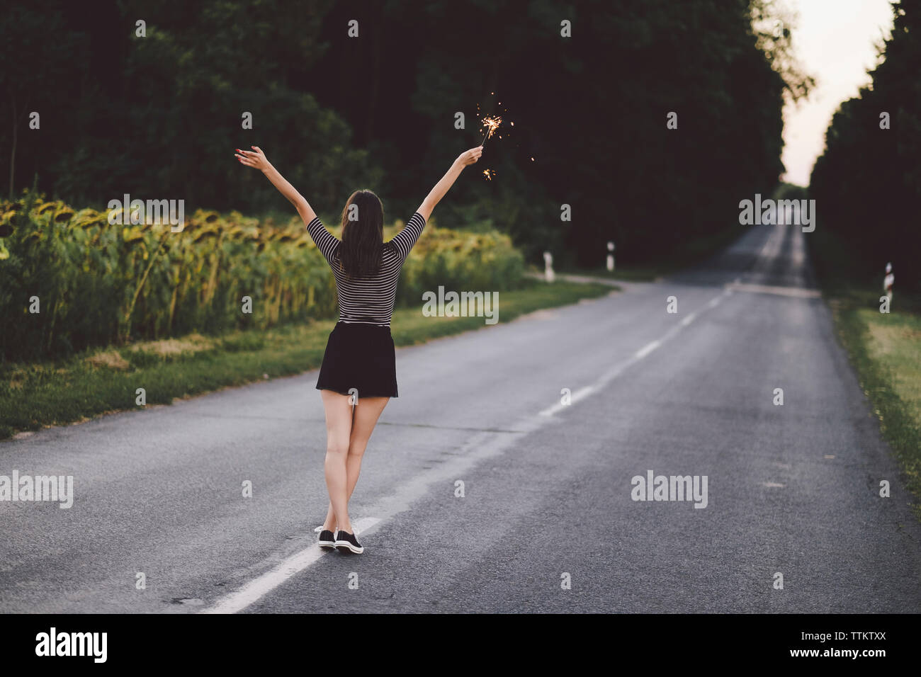 Rear view of woman with arms raised holding sparkler while standing on road Stock Photo