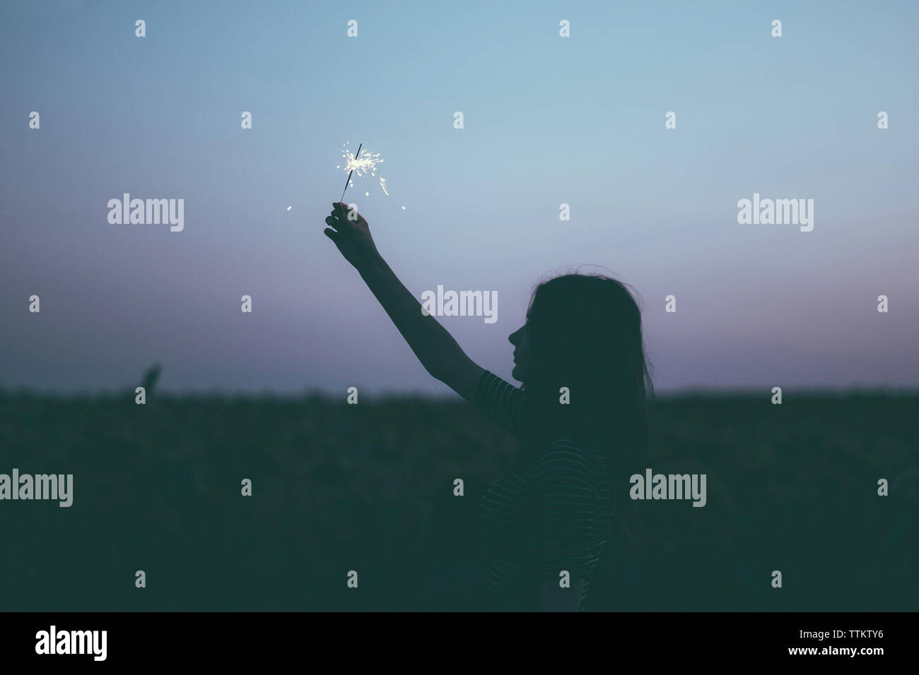 Side view of silhouette woman holding sparkler while standing against sky at dusk Stock Photo