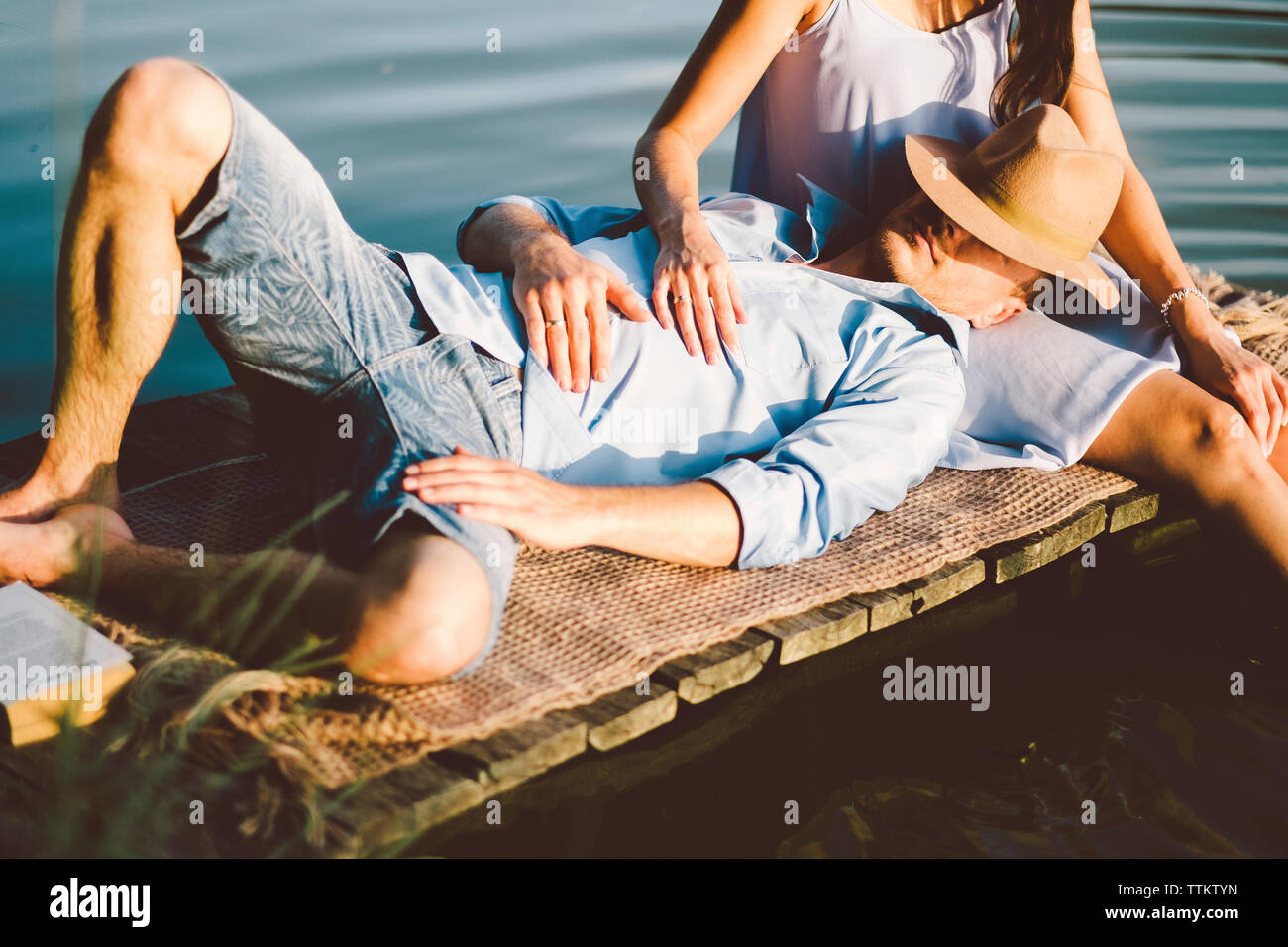 Midsection of girlfriend with boyfriend lying on lap sitting by lake at park Stock Photo