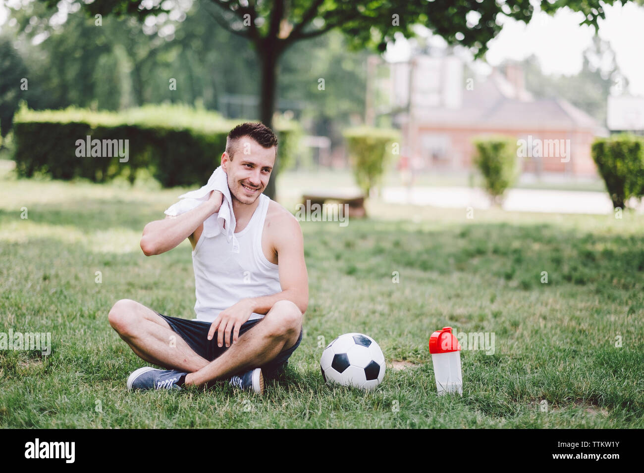 Smiling young man wiping neck while sitting on soccer field at park Stock Photo