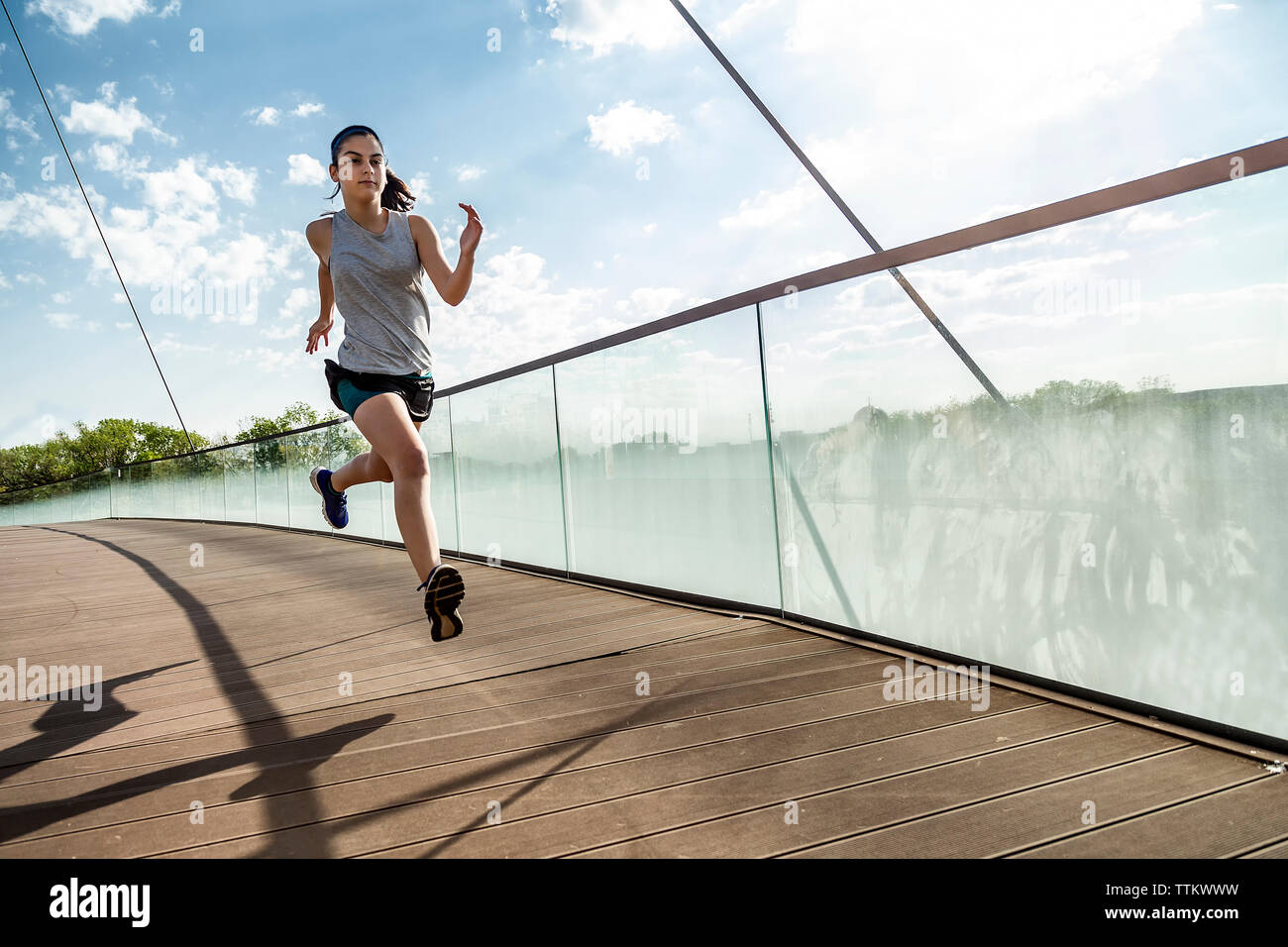 Female athlete running on bridge against sky Stock Photo