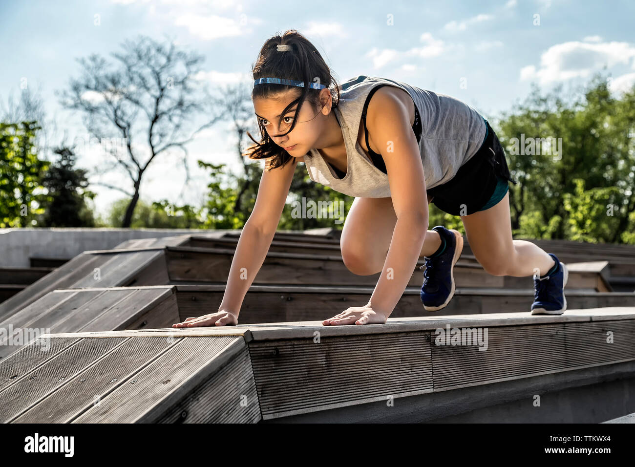 Female athlete exercising on wooden seat against sky Stock Photo