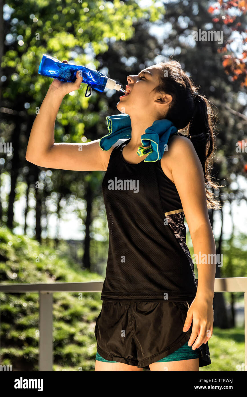 Female athlete drinking water at park during sunny day Stock Photo