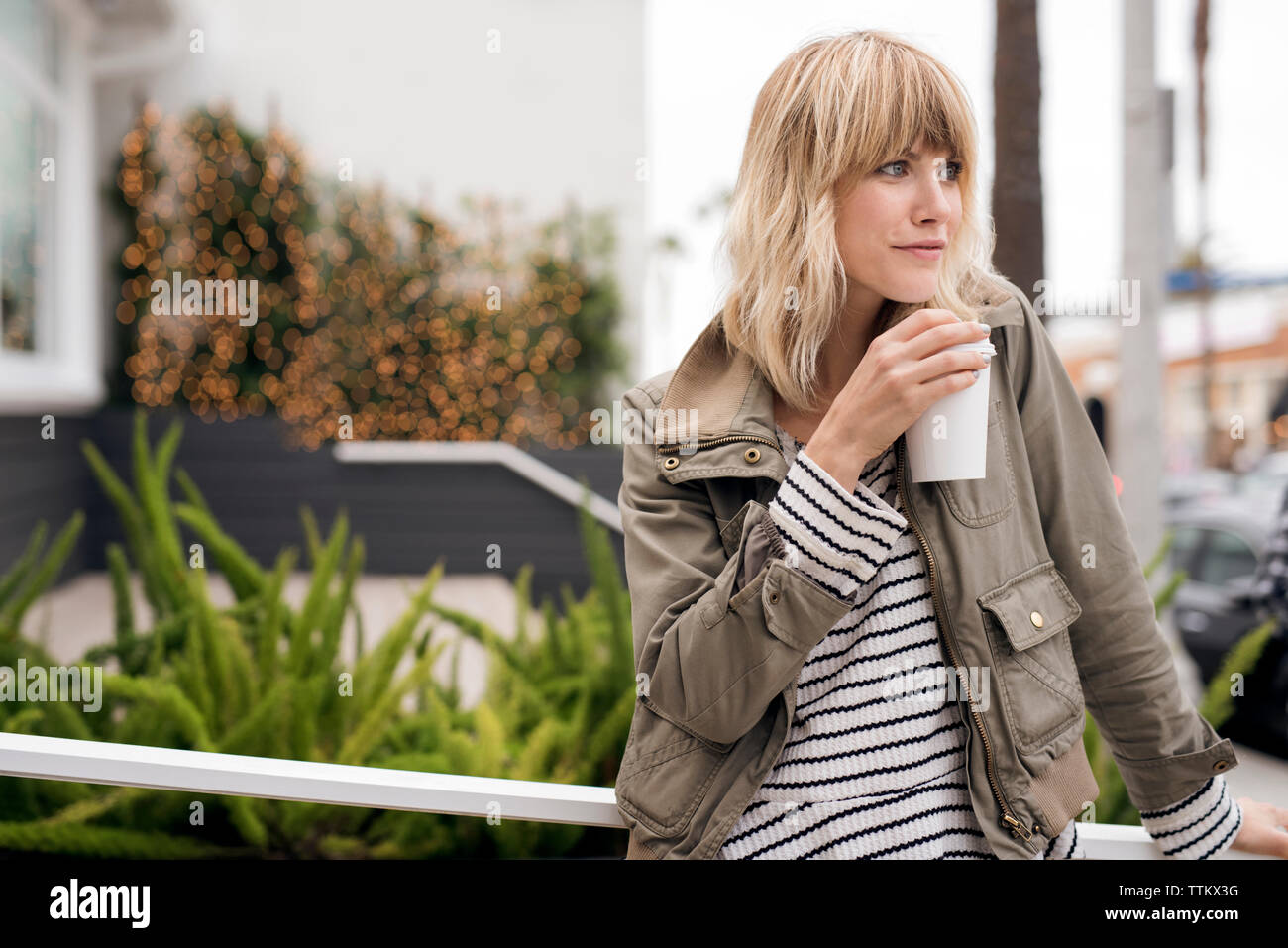 Thoughtful young woman drinking coffee outdoors Stock Photo