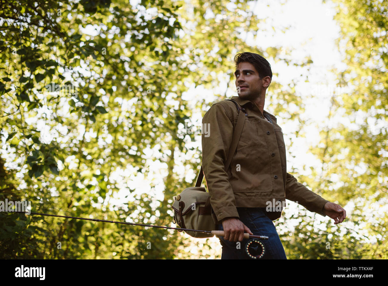 Man looking over shoulder while walking with fishing rod in forest Stock Photo