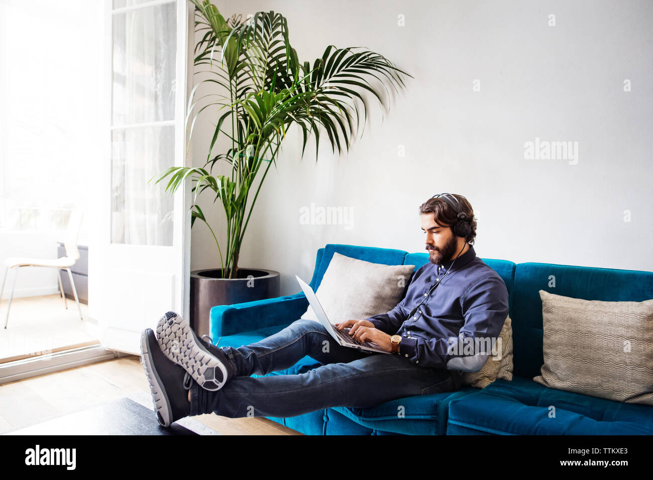 businessman listening music while using laptop on sofa in office Stock Photo