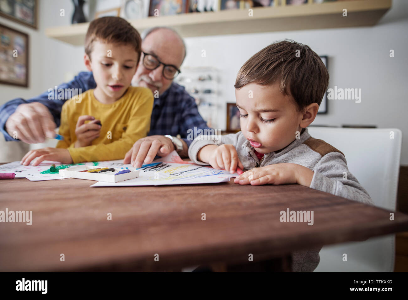 Senior man assisting grandsons in making drawings at home Stock Photo