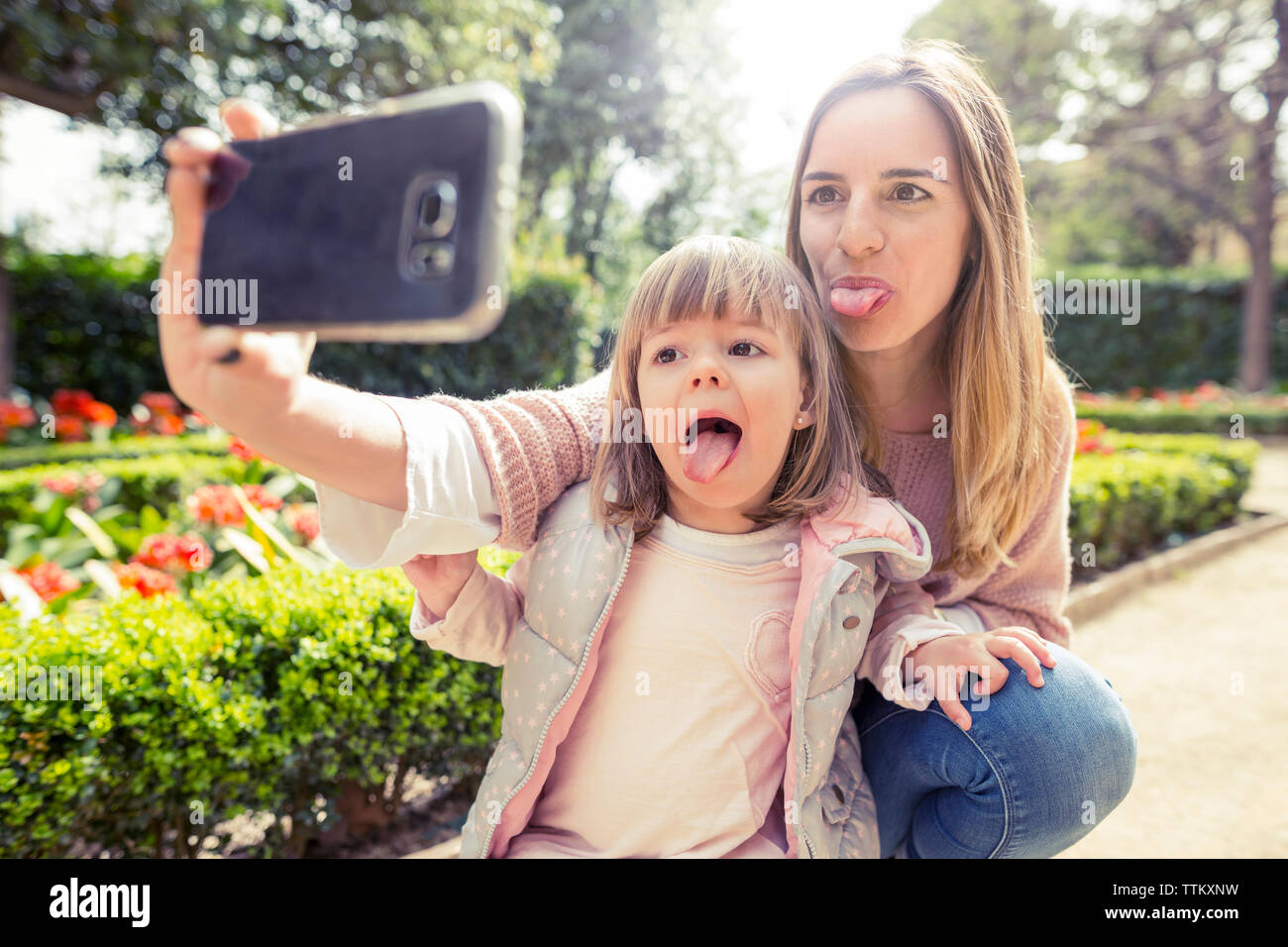Mother and daughter sticking out tongue while taking selfie in park Stock Photo