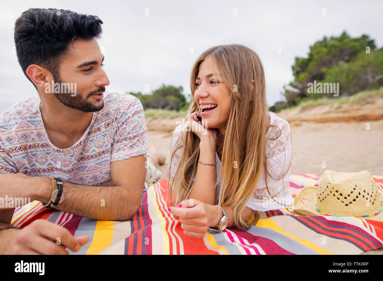 Cheerful couple talking while lying on blanket at beach Stock Photo