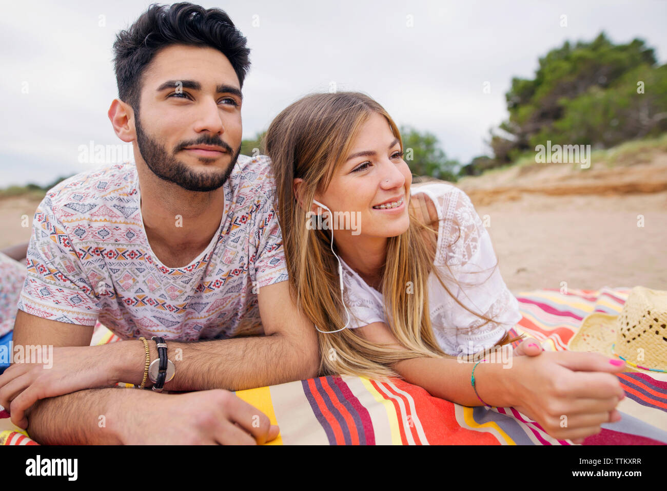 Thoughtful couple looking away while lying on blanket at beach Stock Photo