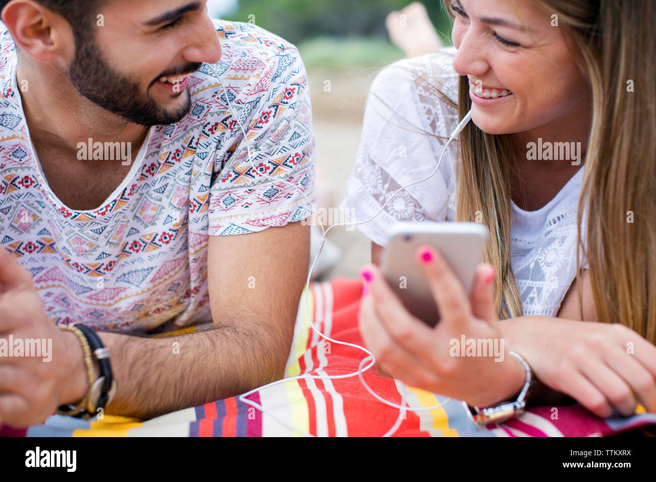 Happy couple looking at each other while lying on blanket at beach Stock Photo