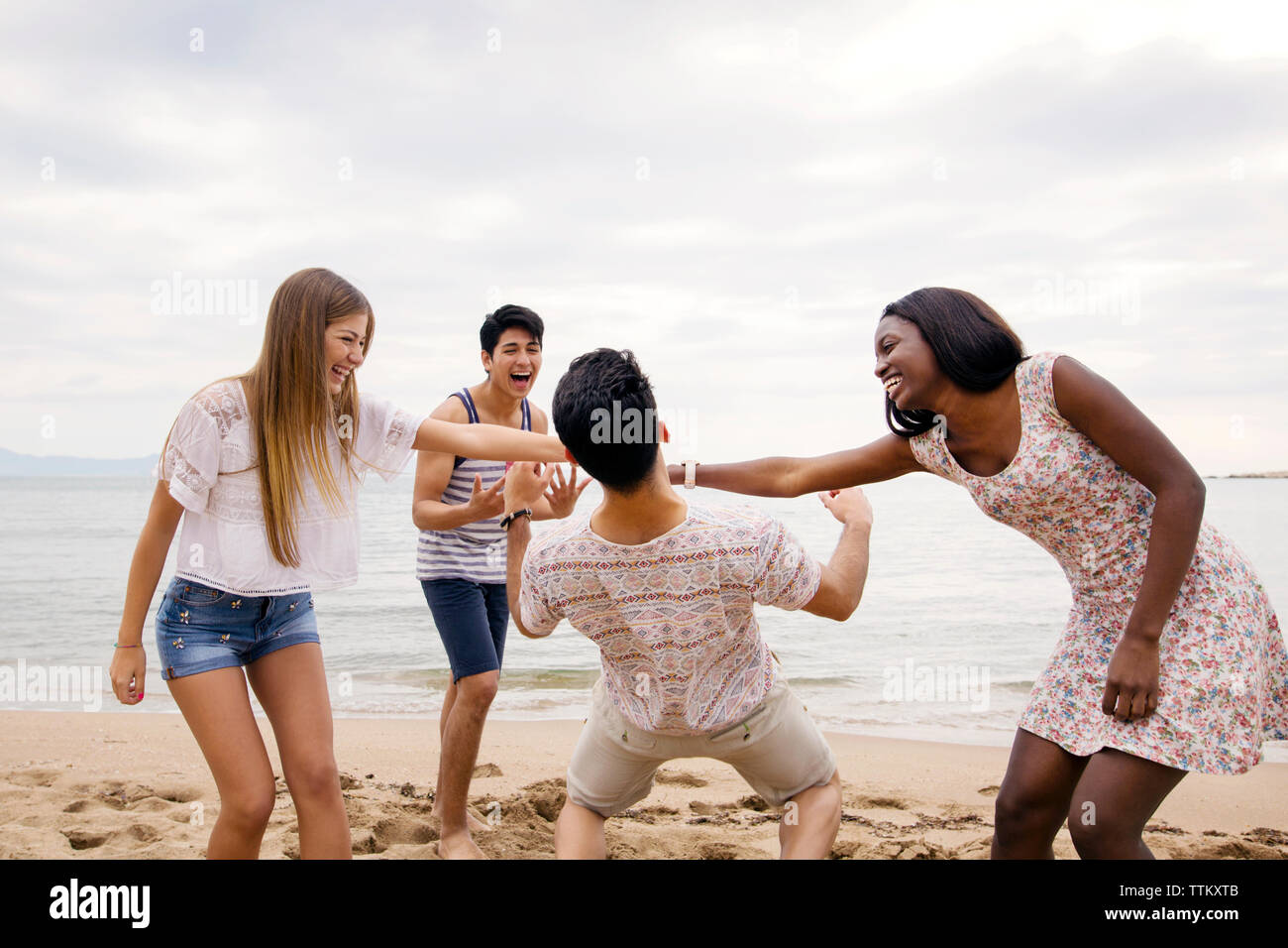 Man passing under women's arms while playing on beach against sky Stock Photo