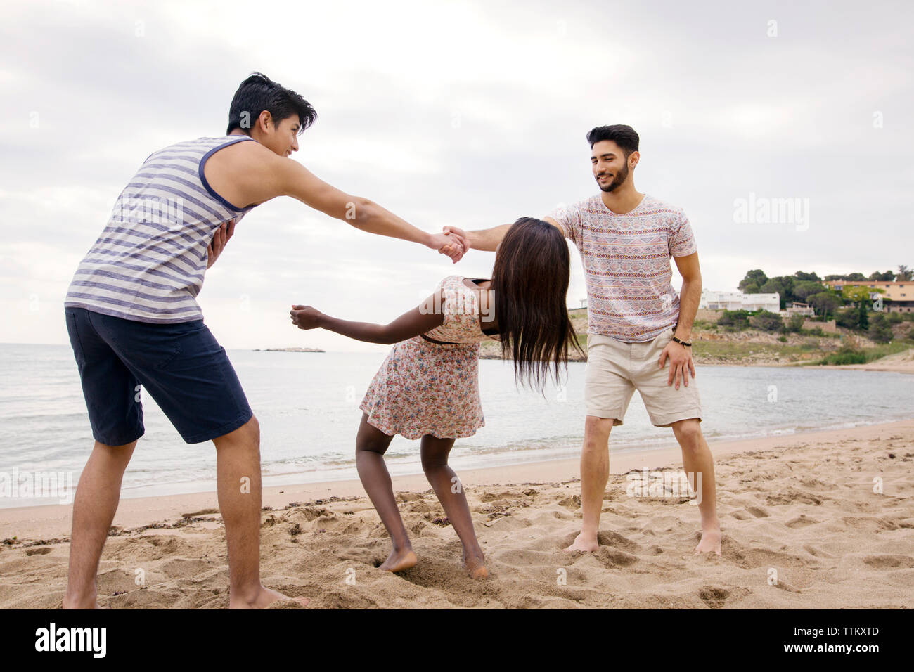 Woman passing under men's arms while playing on beach Stock Photo