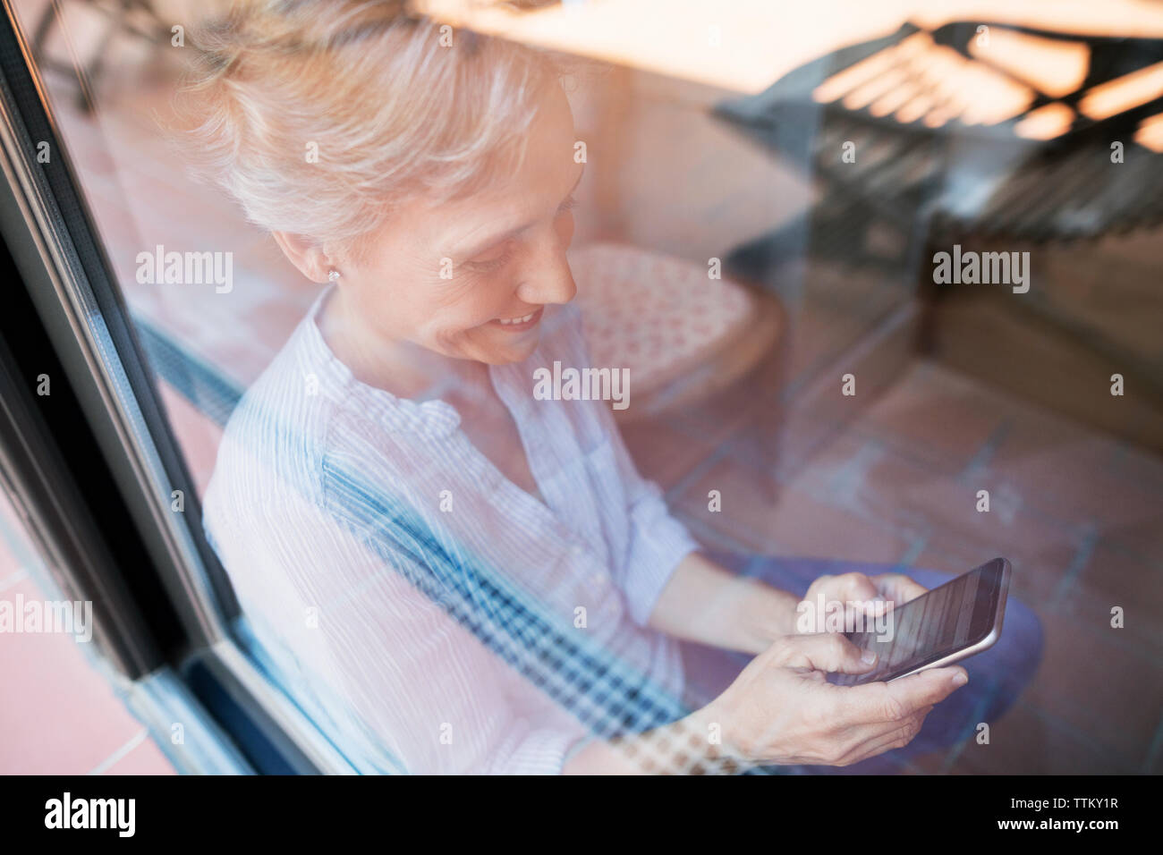 Mature woman using smart phone seen through glass window Stock Photo