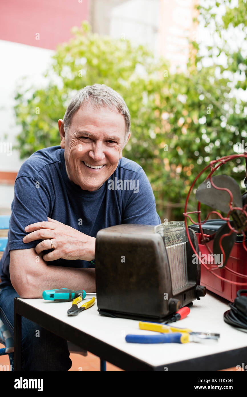 Portrait of happy senior man repairing vintage radio at yard Stock Photo