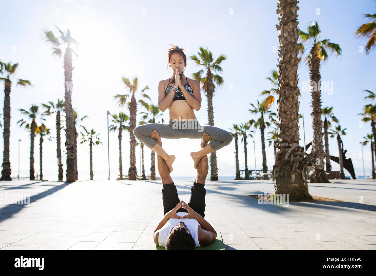 Couple performing yoga on footpath at beach during summer Stock Photo