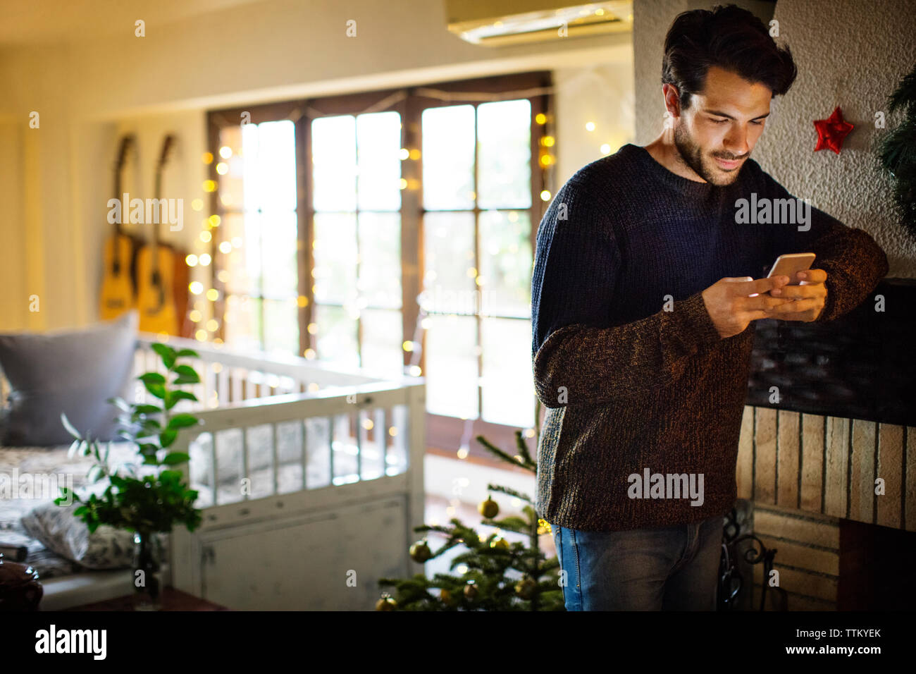 Thoughtful man using smart phone while standing at home during christmas Stock Photo