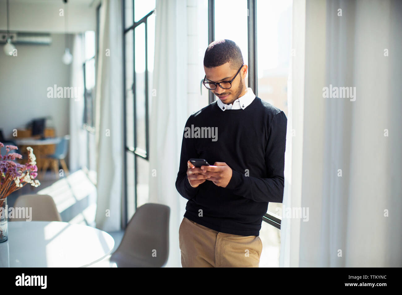 businessman using mobile phone while standing by window at office Stock Photo