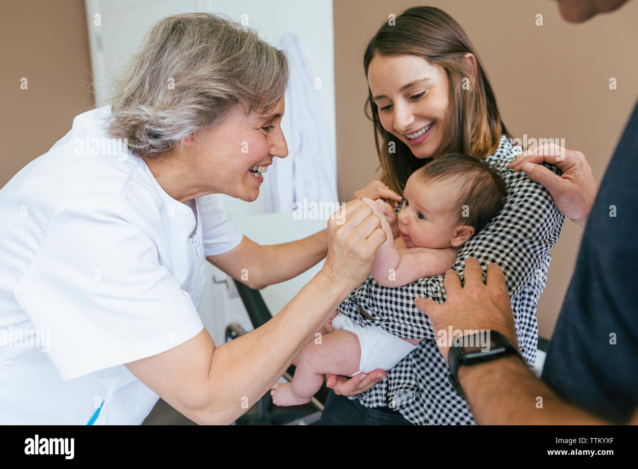 Smiling mother looking at doctor playing with baby boy in examination room Stock Photo