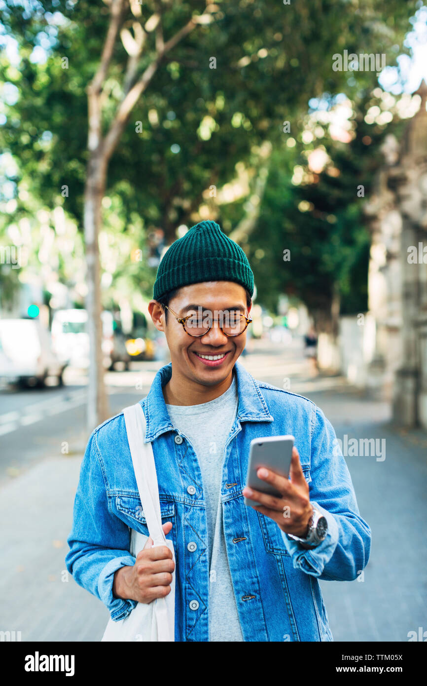 Happy man using smart phone while standing at sidewalk Stock Photo