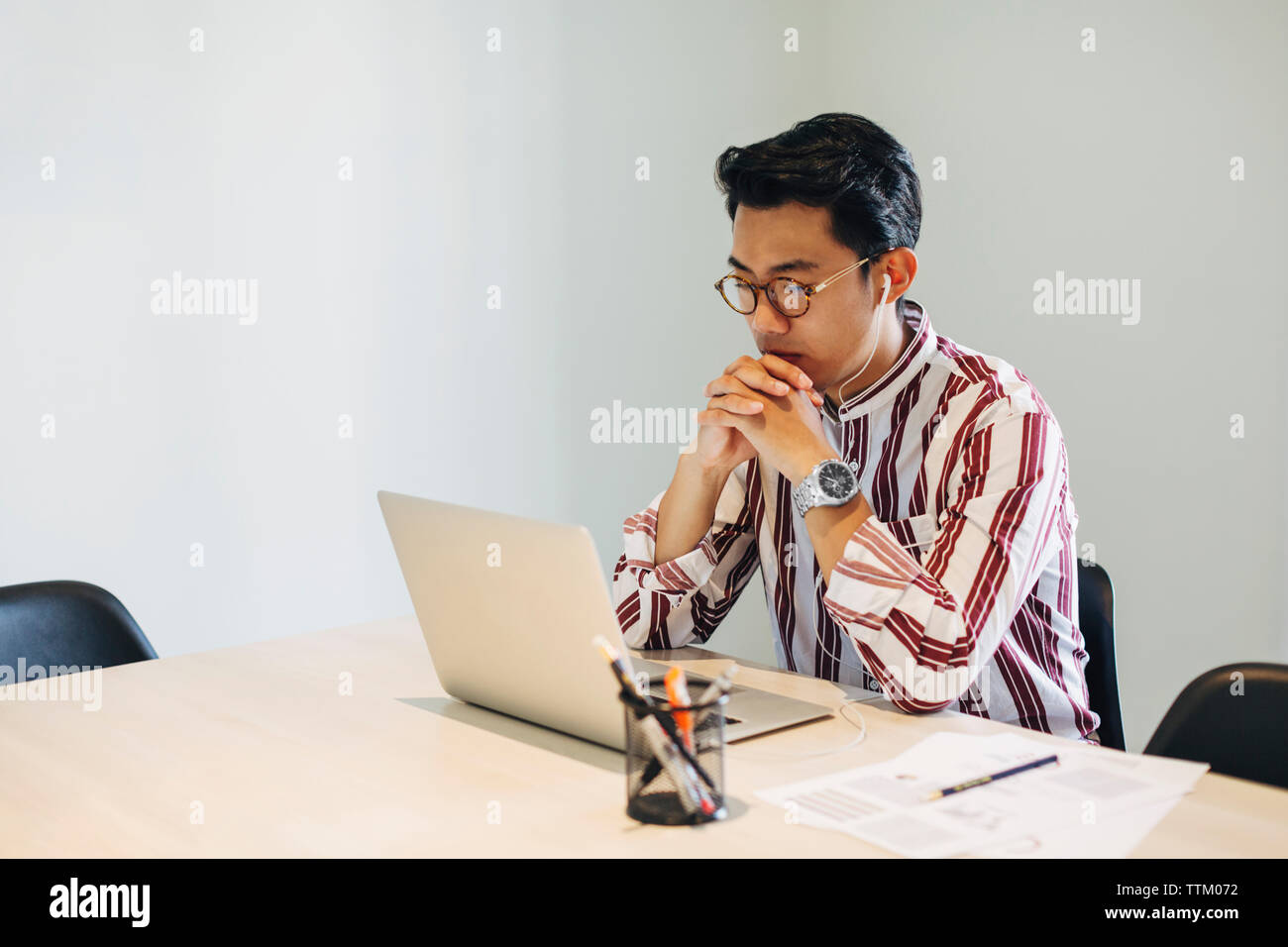 Serious businessman with hands clasped looking at laptop computer while sitting in board room Stock Photo