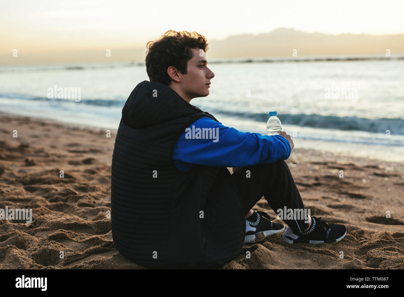 https://c8.alamy.com/comp/TTM087/side-view-of-thoughtful-teenage-boy-holding-water-bottle-while-sitting-at-beach-TTM087.jpg