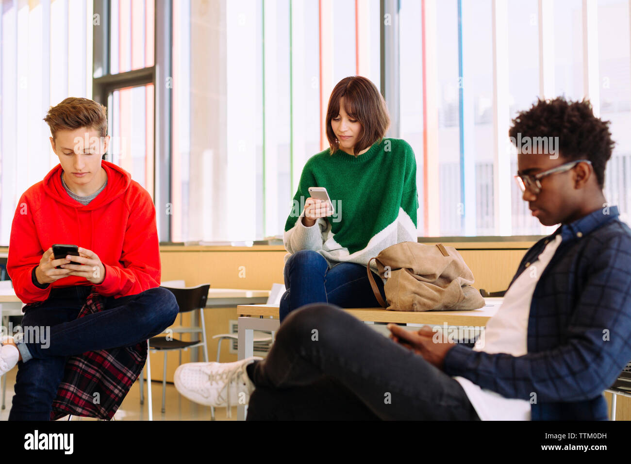 students using mobile phones while sitting in library Stock Photo