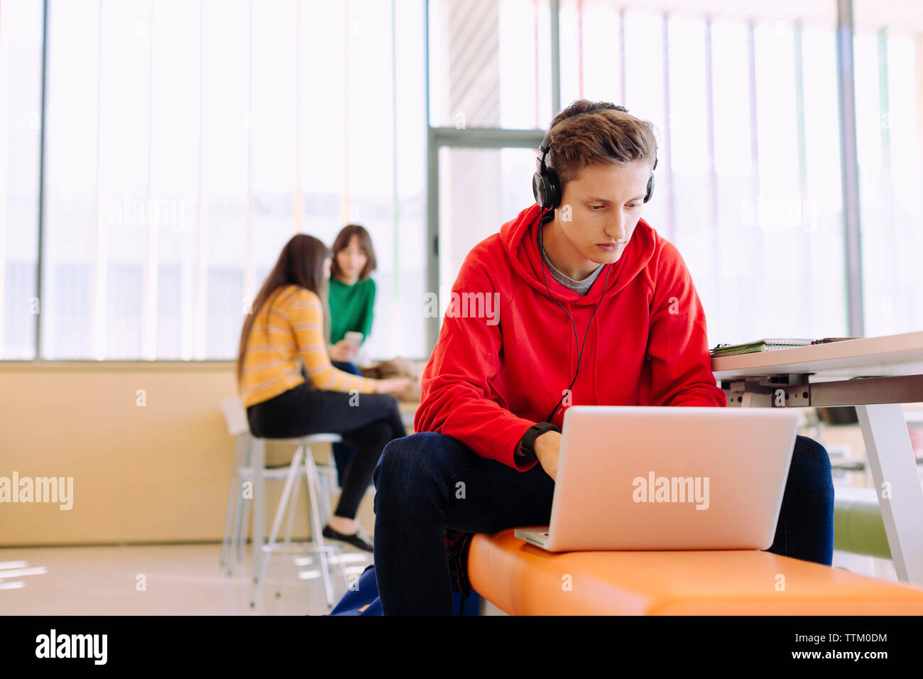 Man using laptop while female friends studying in background at library Stock Photo
