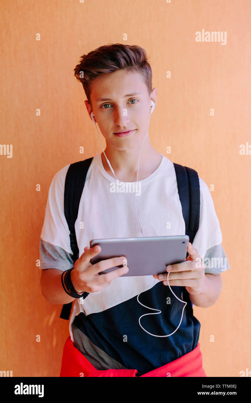 Portrait of man using tablet computer while standing against orange wall at library Stock Photo