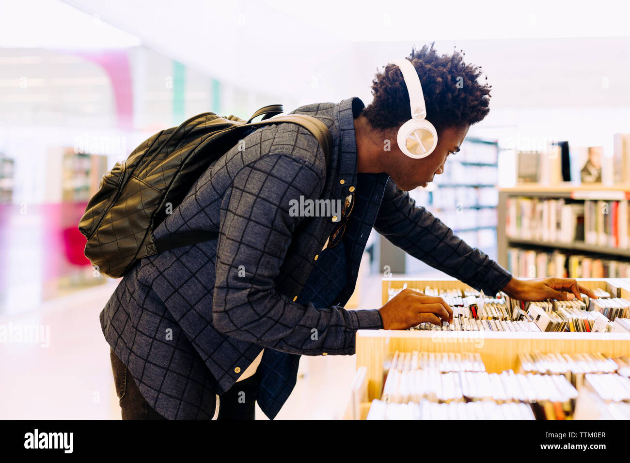 Side view of man searching books in shelf at library Stock Photo