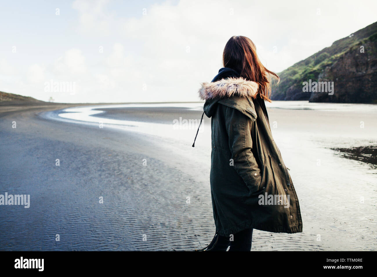 Side view of woman standing at Bethells Beach on sunny day Stock Photo