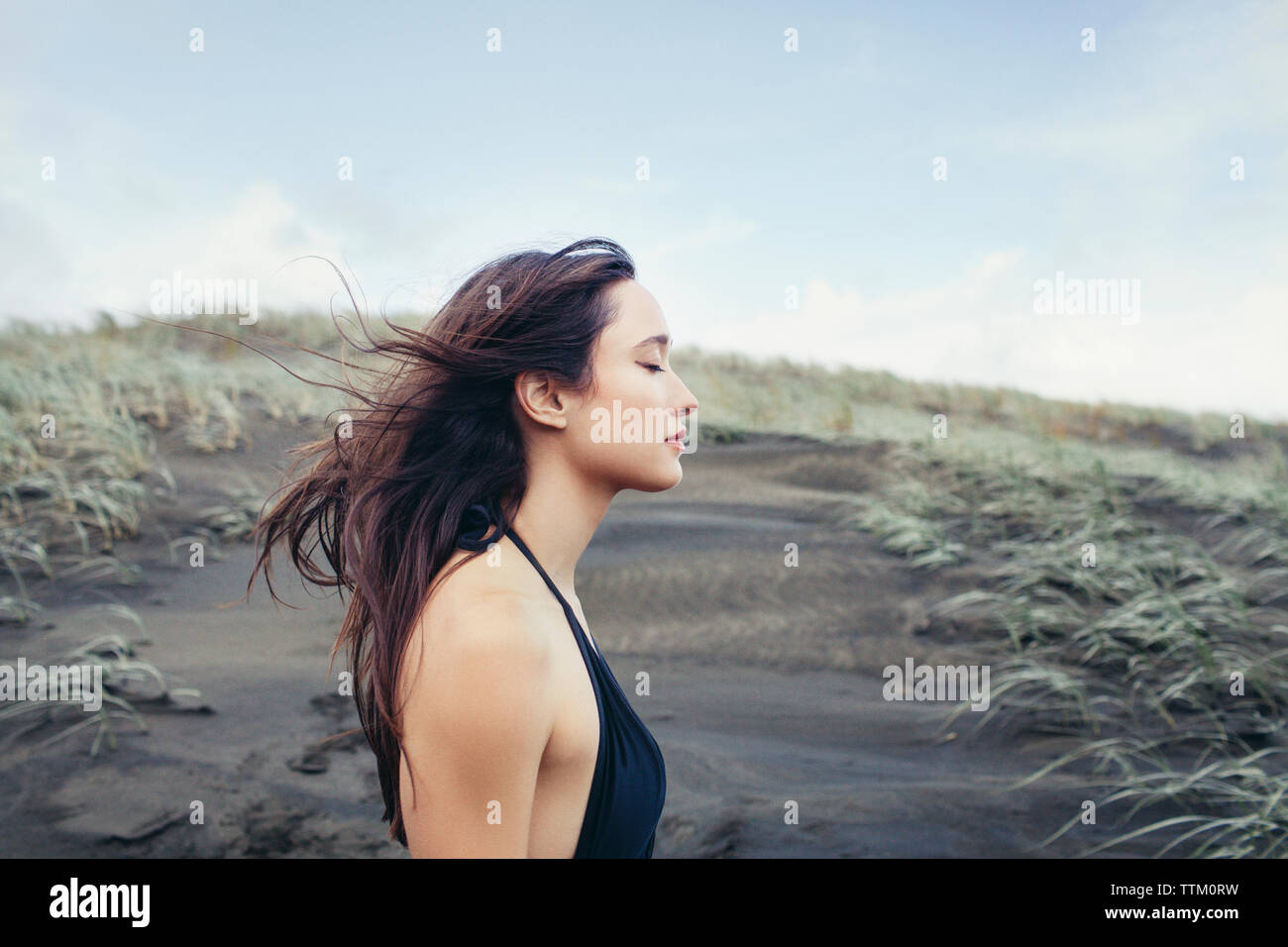 Side view of woman enjoying breeze at Bethells Beach against sky Stock Photo