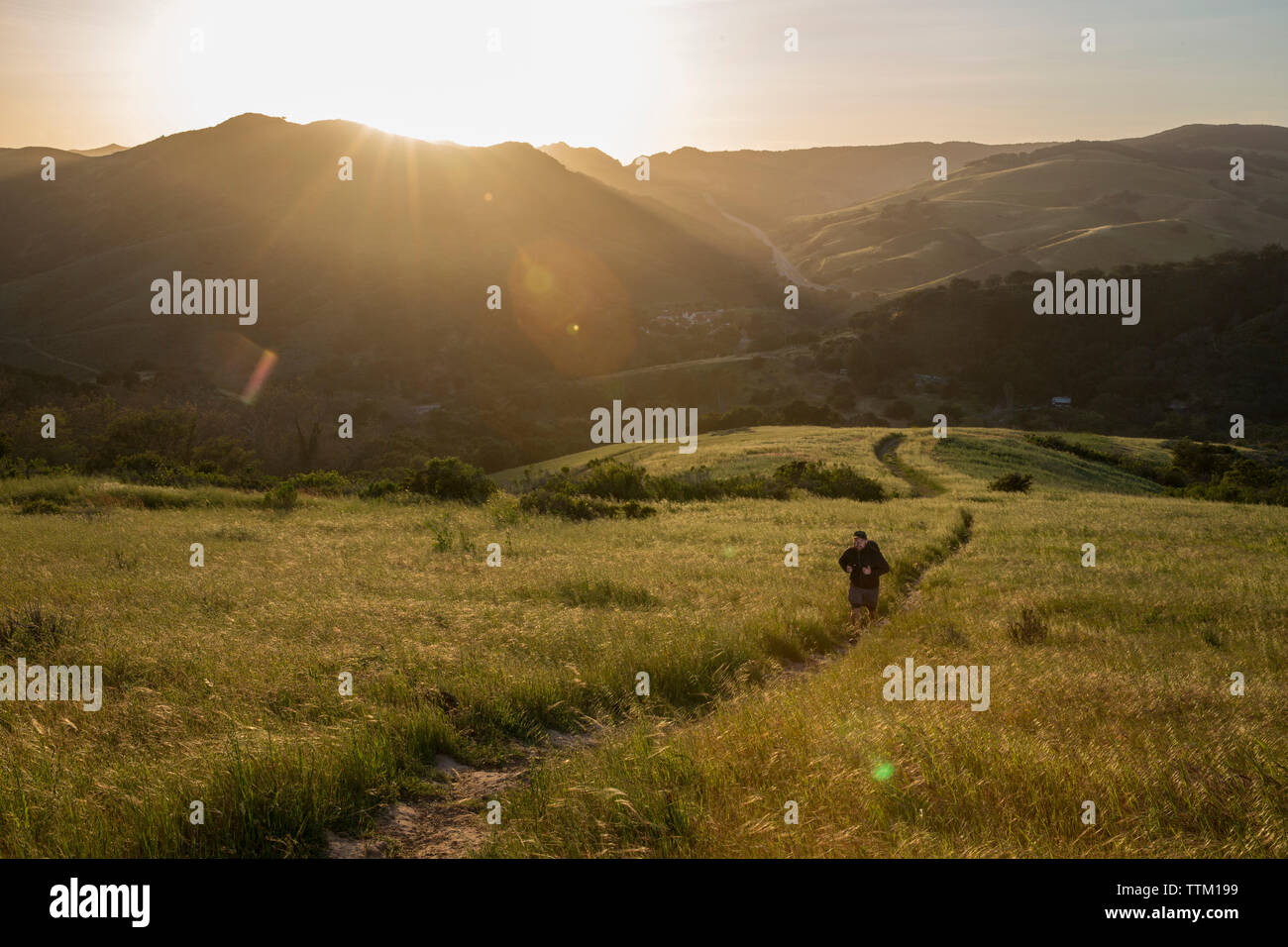 High angle view of man on trail amidst grassy field against mountains during sunset Stock Photo