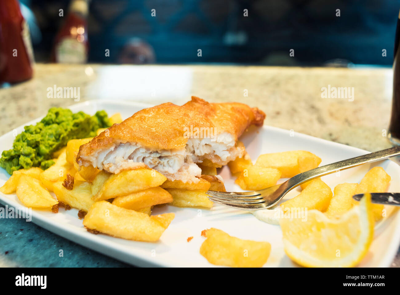 Close-up of fish with French fries and lemon slice in plate on table at restaurant Stock Photo