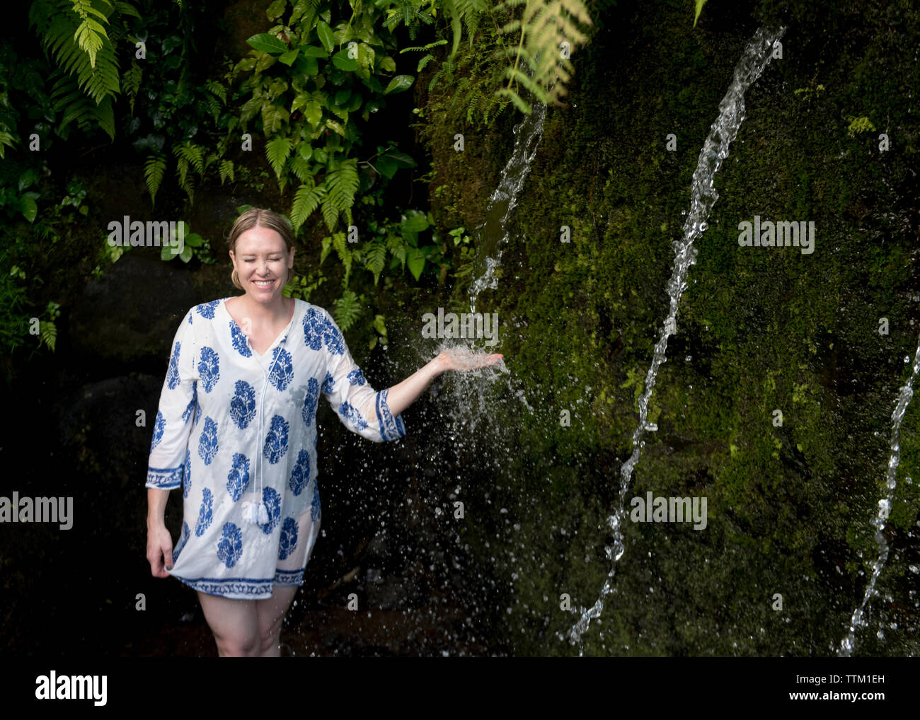 Carefree female tourist enjoying in waterfall at forest Stock Photo
