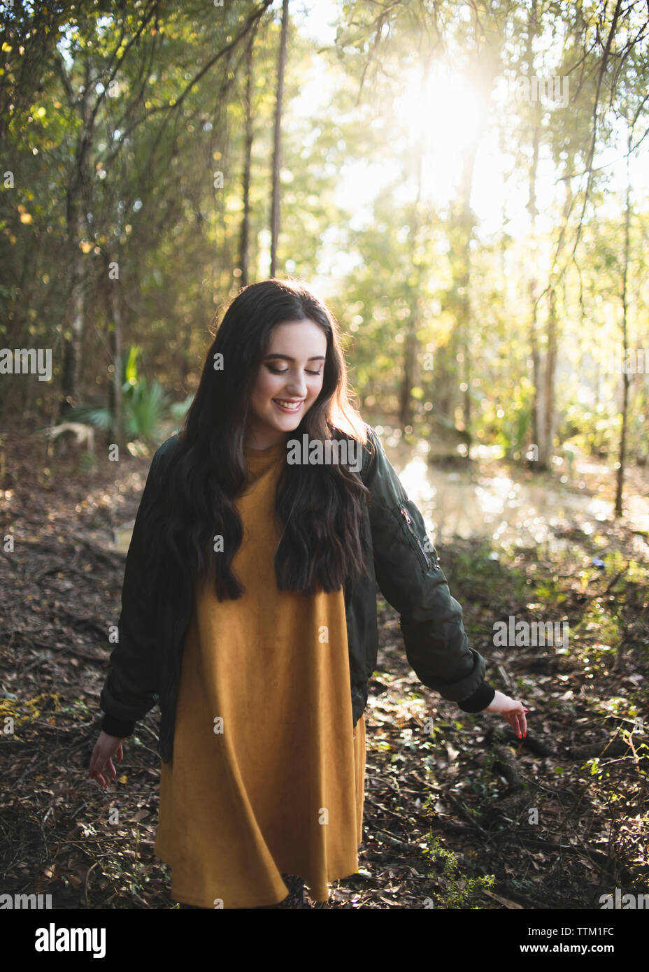 Happy teenage girl looking down while walking against trees in forest