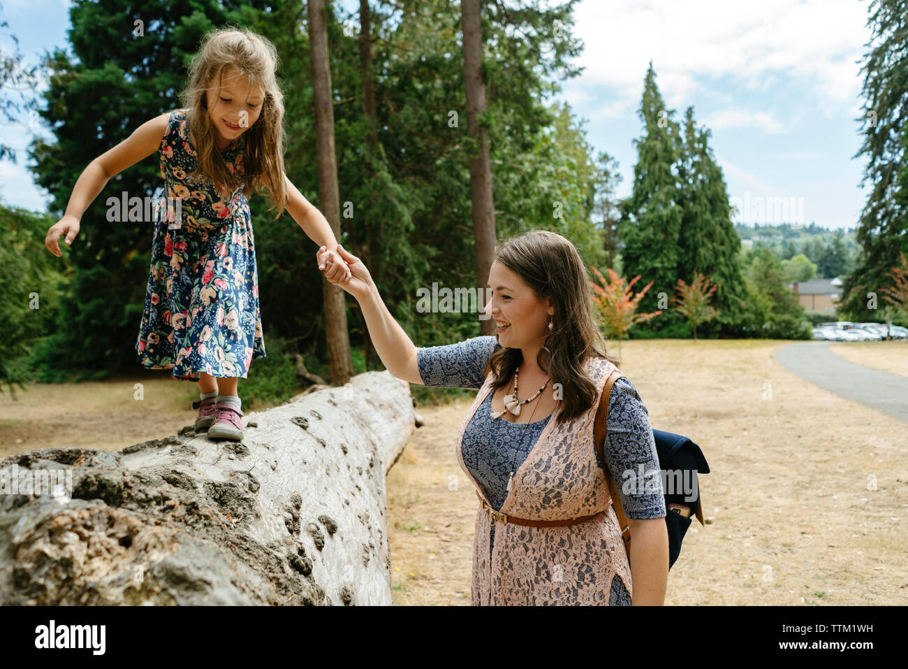 Mother assisting cute daughter in walking on log against trees at forest Stock Photo