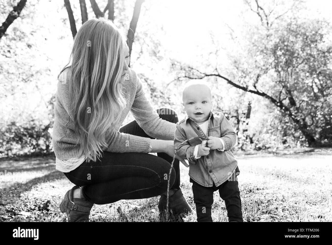 A mom helps her baby son stand outdoors Stock Photo