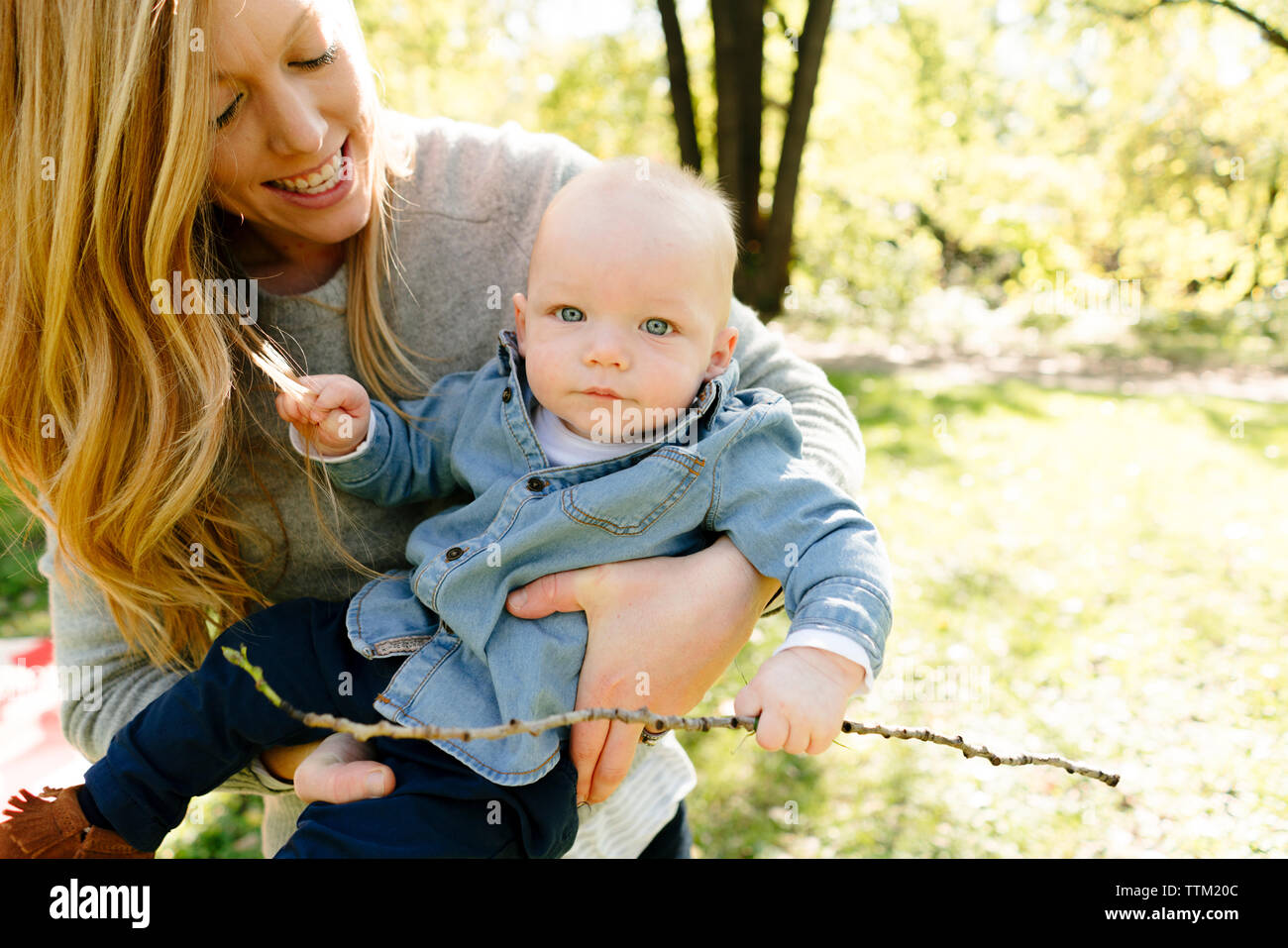 A mom holds her baby son while he holds a stick Stock Photo